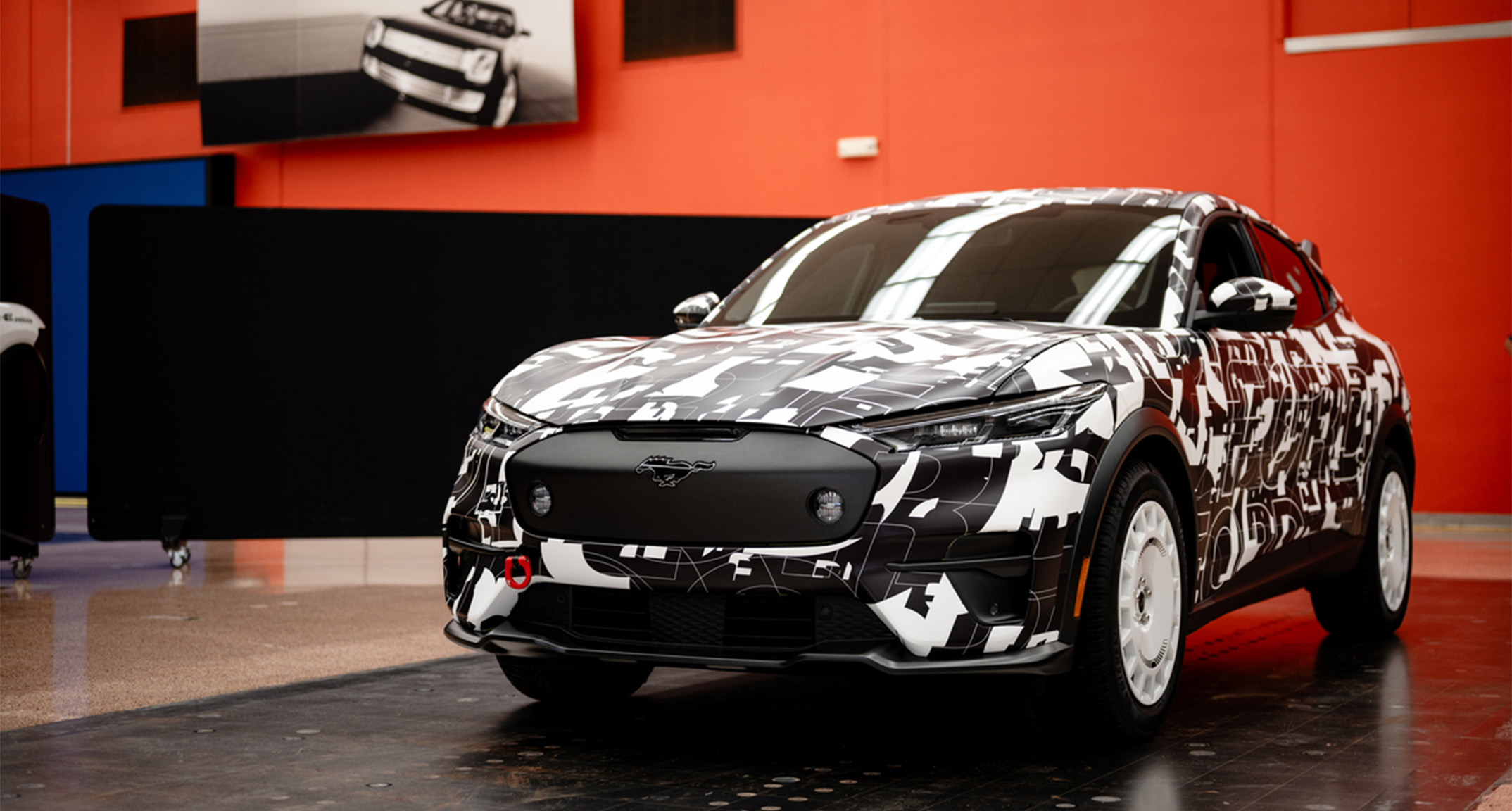 The Mustang Mach-E Rally, which has an artistic black and white exterior, contrasts with the bright orange walls of a showroom. 
