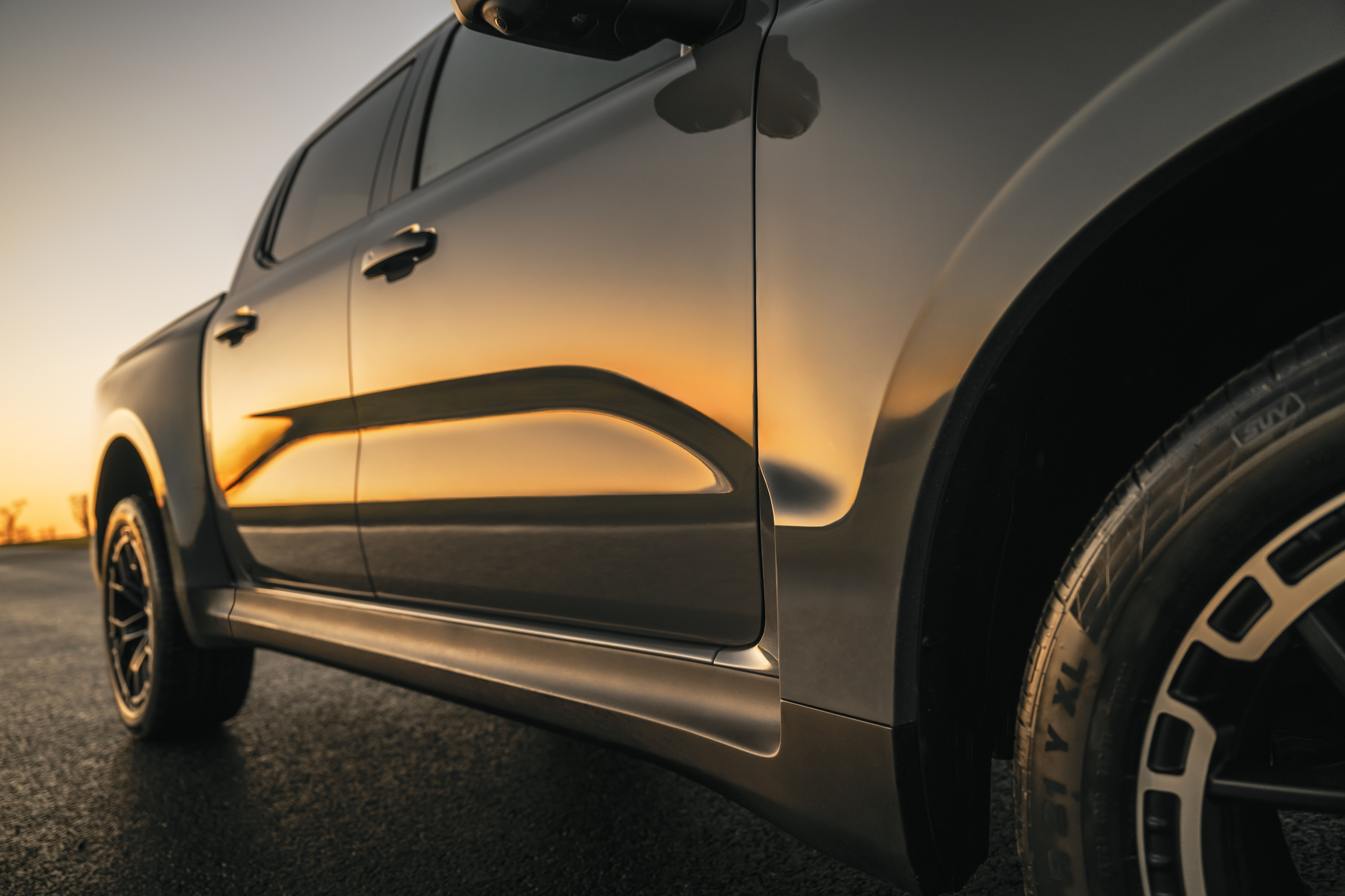 A closeup of a grey pickup reflecting a sunset