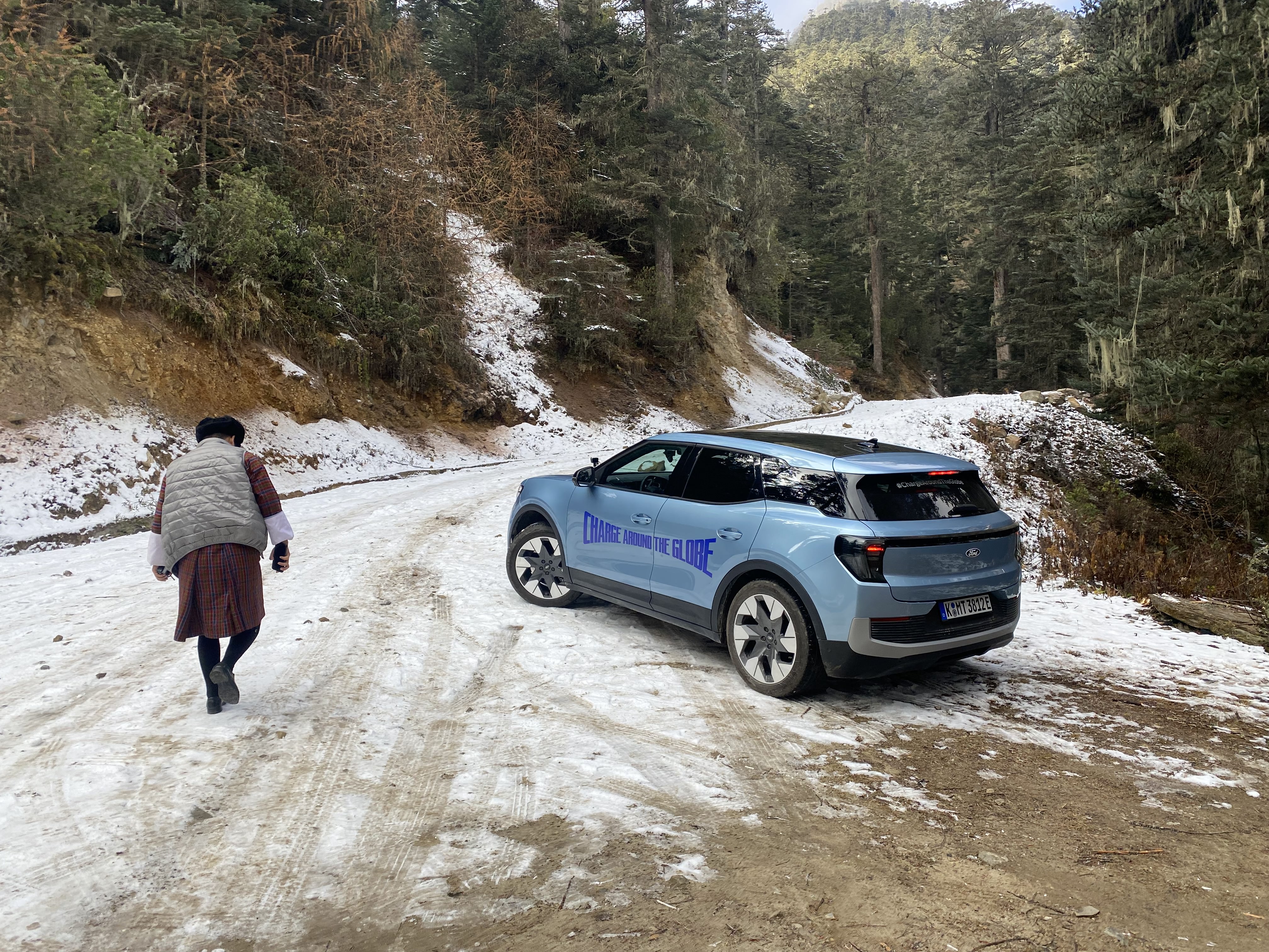 A car in a snowy environment with a woman walking nearby
