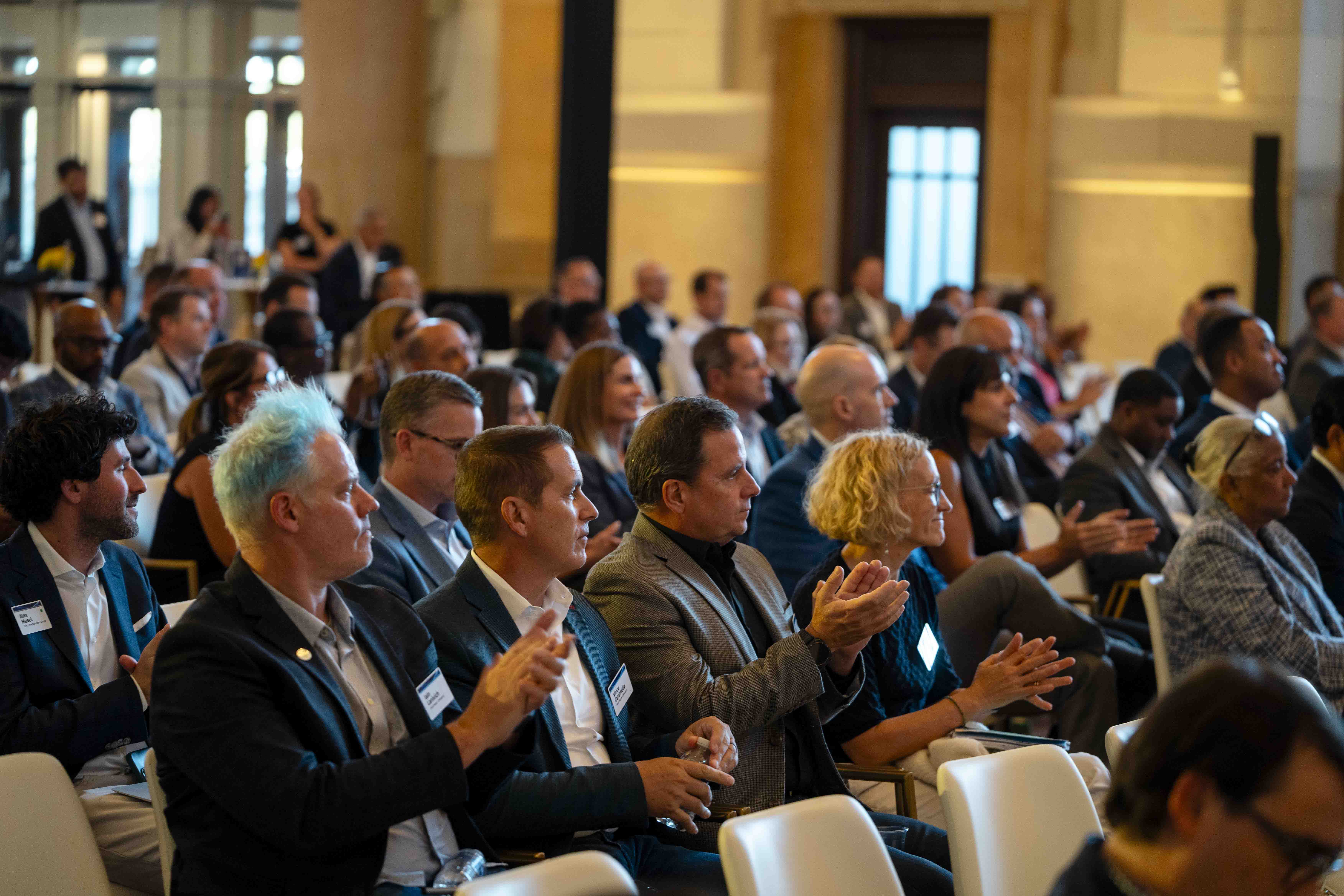 An audience mostly dressed in business attire looks toward the stage and claps