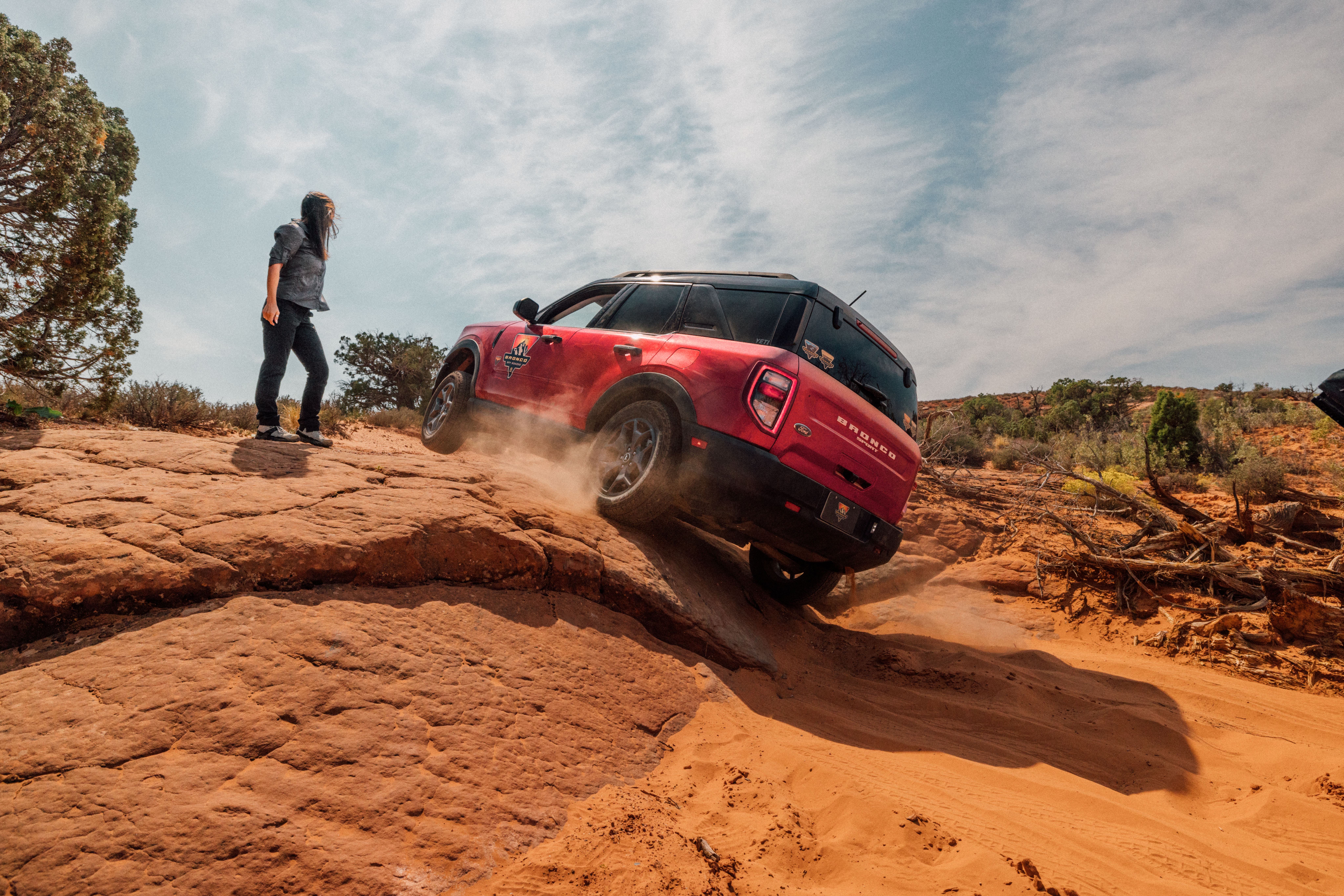 A red Ford Bronco climbs over red rocks