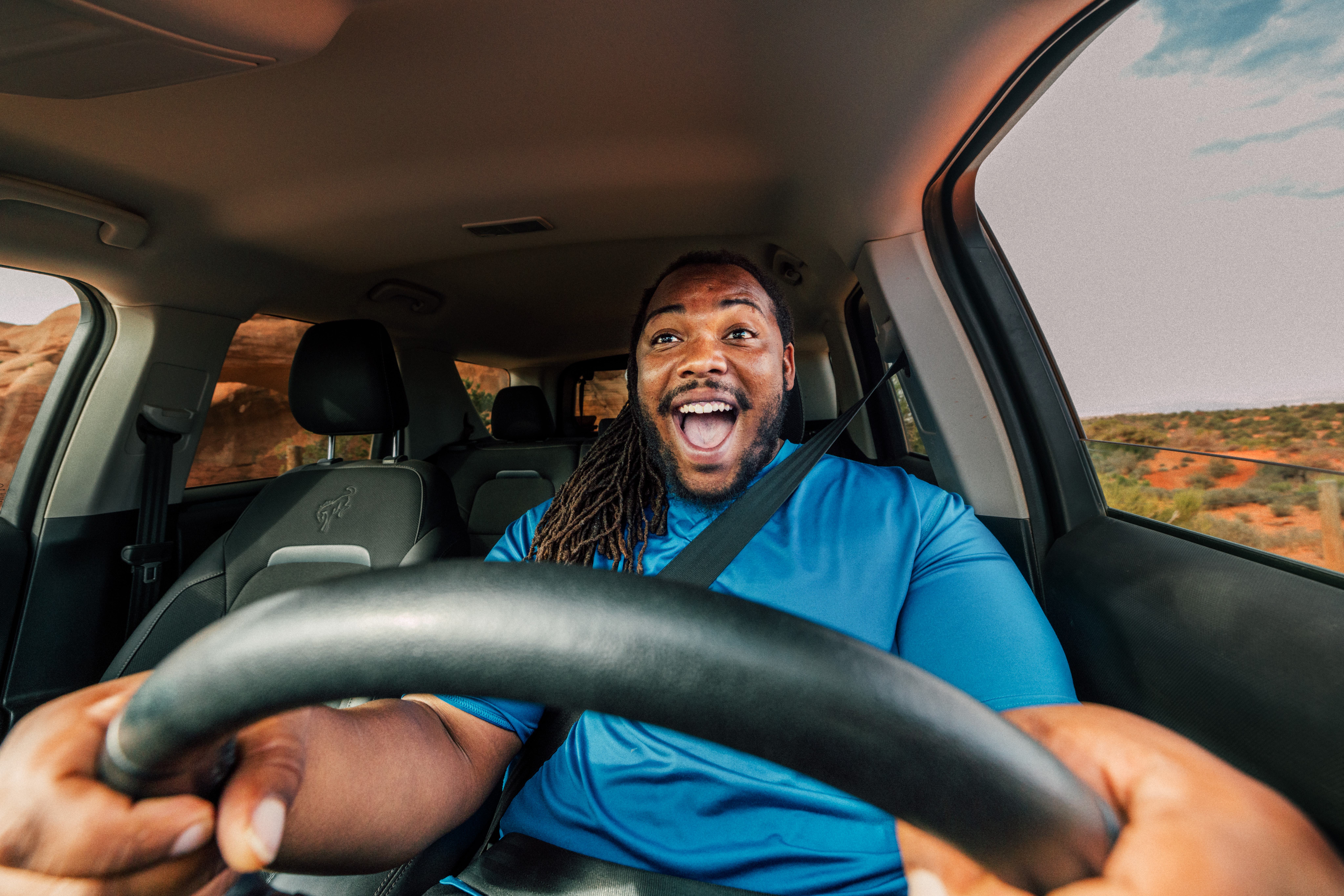 Shown from the dashboard in front of the steering wheel, the man holding the steering wheel of a Ford Bronco has an excited smile on his face.