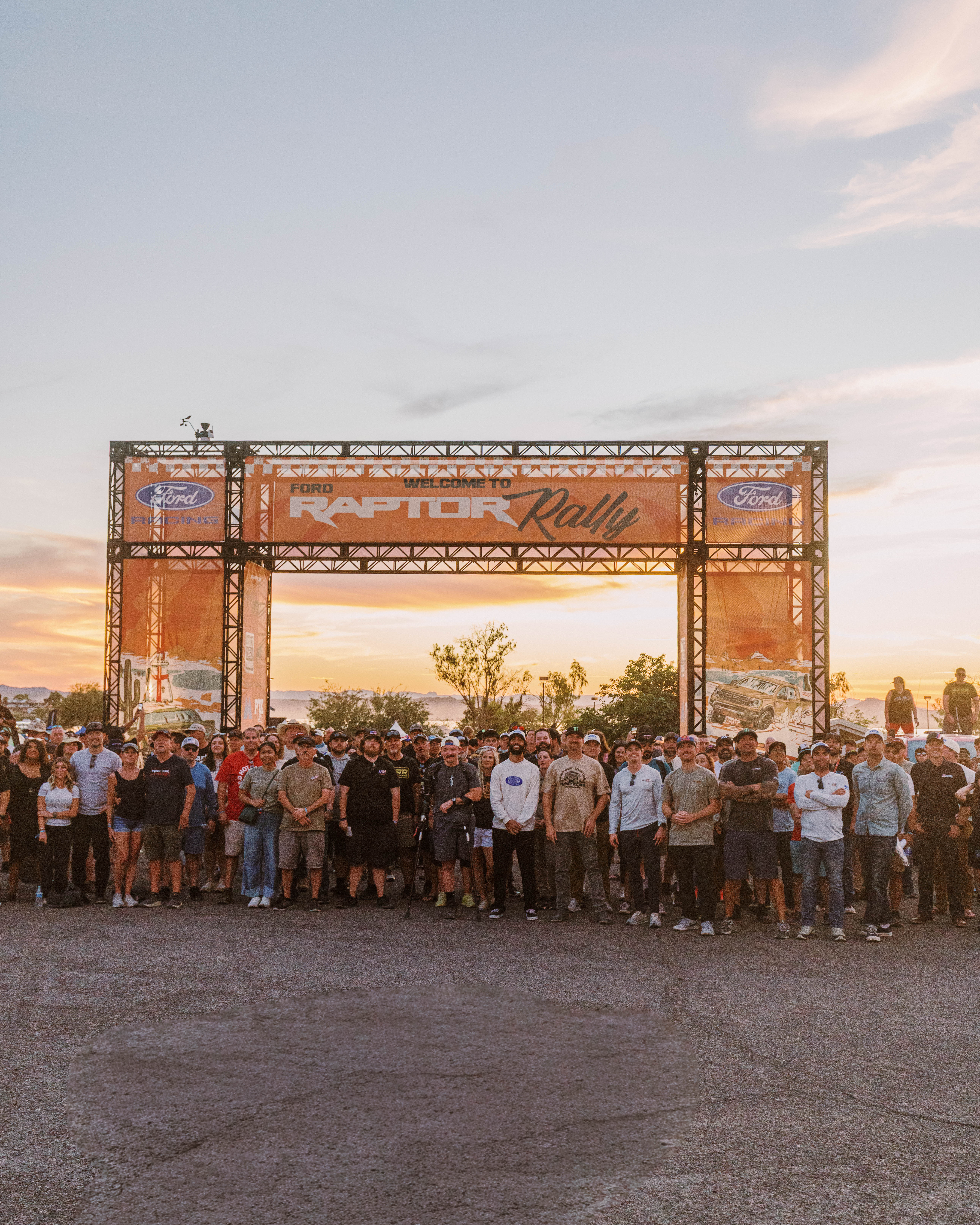 A group of people pose for a photo in front of the setting sun and Raptor Rally sign.
