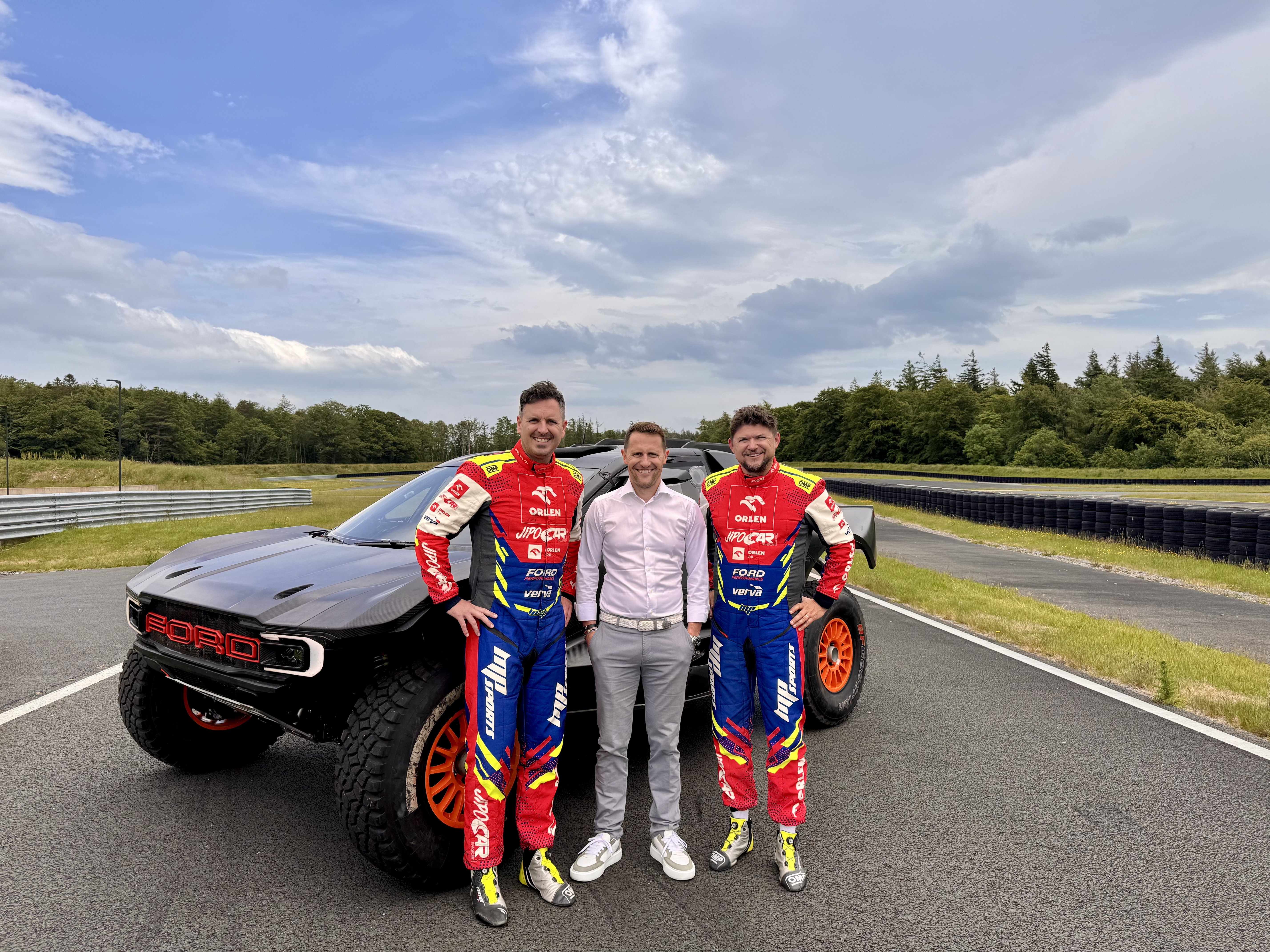 Viktor Chytka (left), Matthew Wilson (center), and Martin Prokop (right) on the grounds of M-Sport with their Ford Raptor T1+.