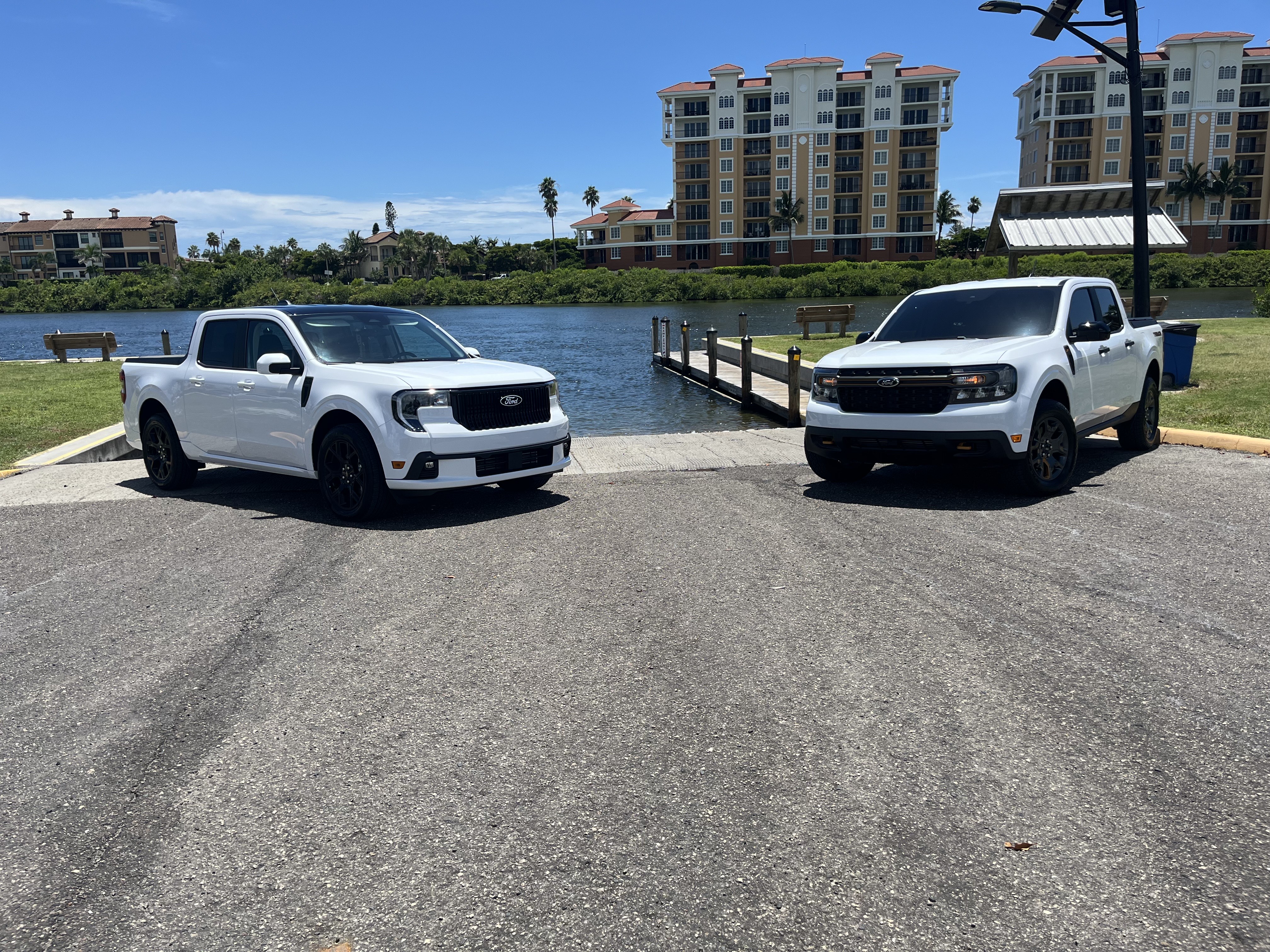 Two white Ford trucks are parked in front of a lake on a sunny day.