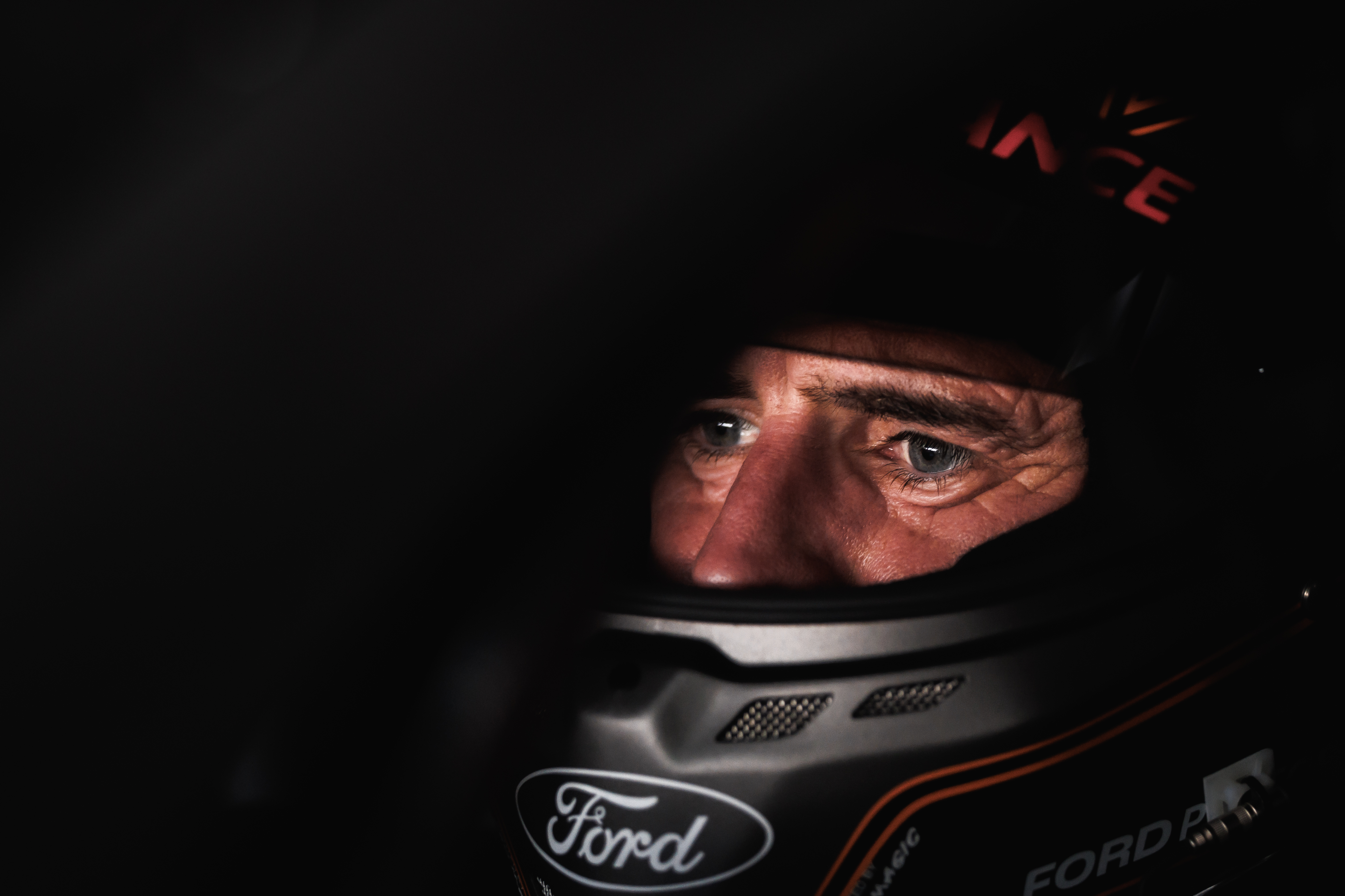 A dark portrait of Ford Performance driver Romain Dumas with his racing helmet on, eyes and nose visible