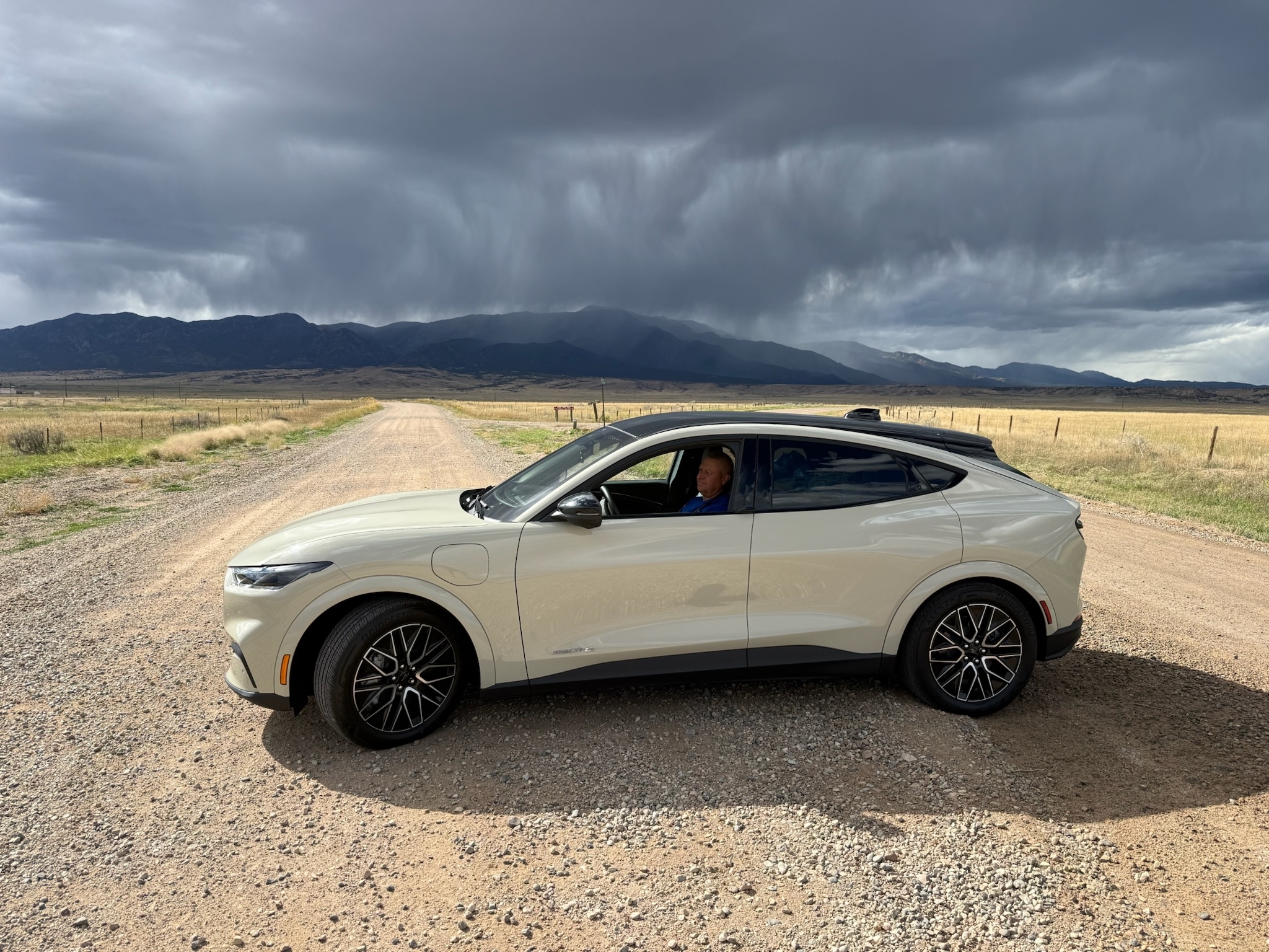A Mustang Mach-E parked on a dirt road with gray clouds overhead.