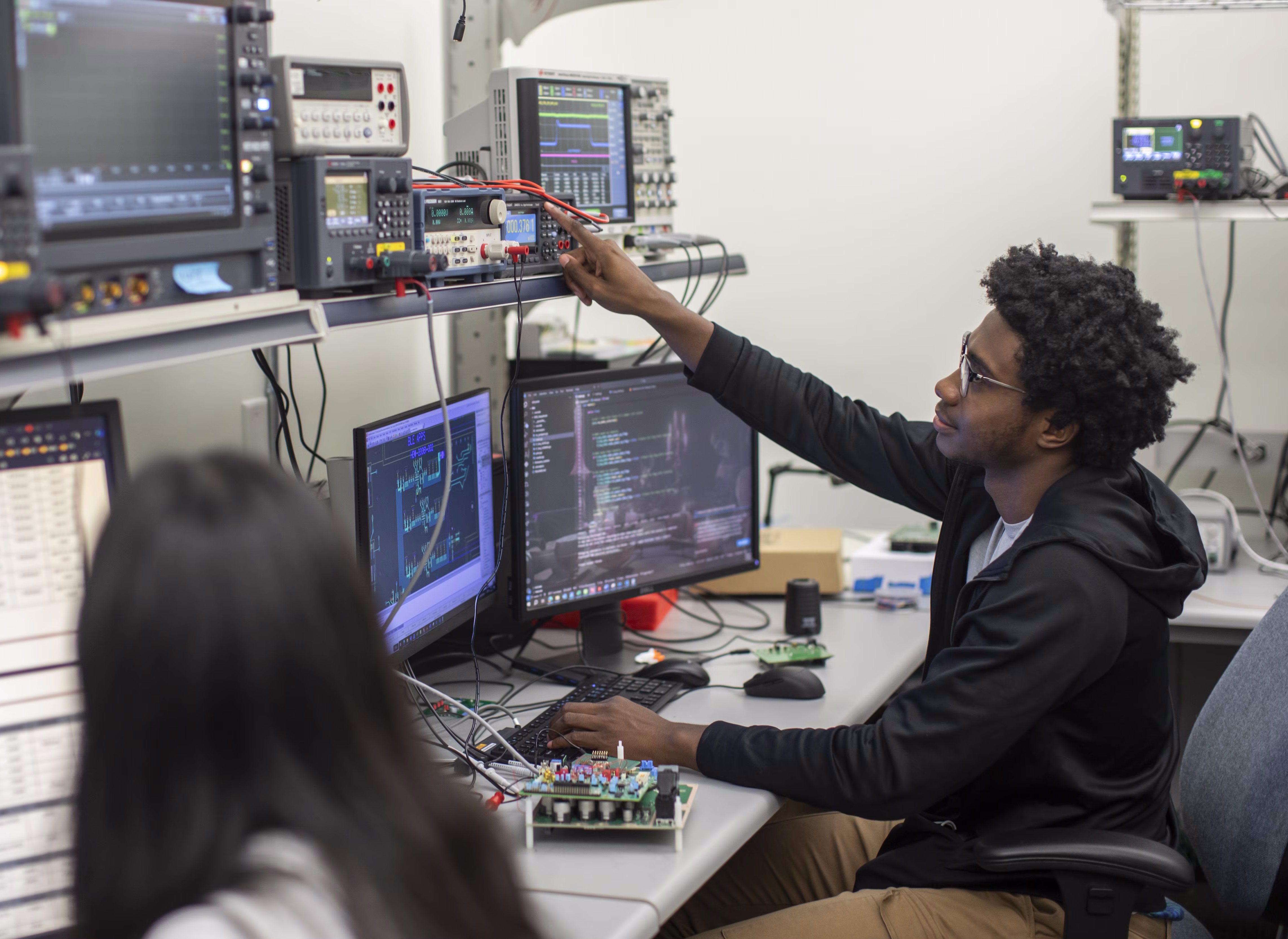 Two engineers sit at a desk with several computer monitors.